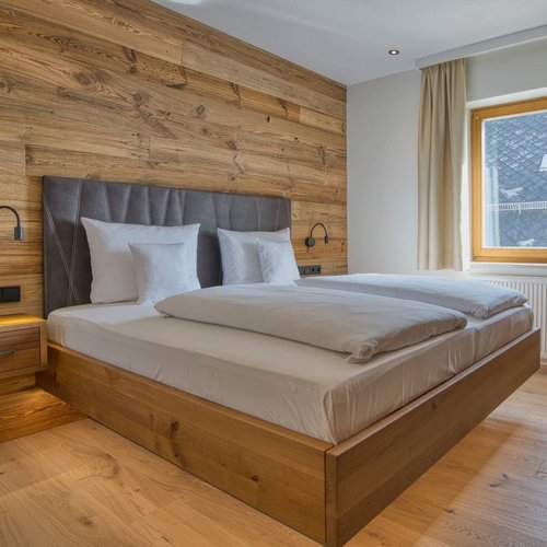 Hotel Hofbräuhaus: freie Stellen Helles zweites Schlafzimmer einer Suite im Wellnesshotel Hofbräuhaus in Bodenmais, ausgestattet mit komfortablem Doppelbett, Holzverkleidung, Fenster mit Blick auf das Dach und die umliegende Natur