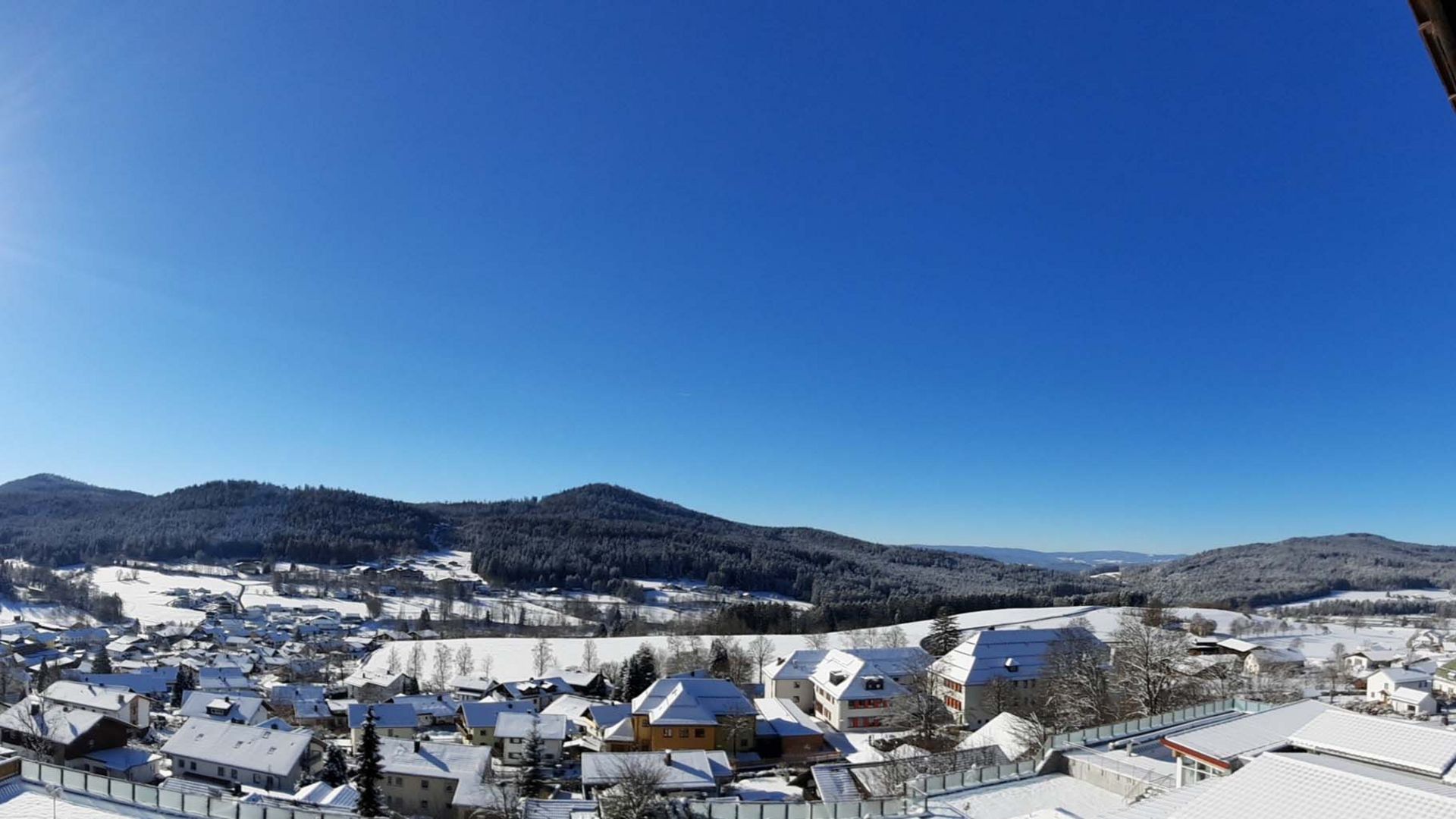 Rund um Bodenmais: Ausflugsziele im Bayerischen Wald Panoramaaufnahme des verschneiten Ortes Bodenmais unter strahlend blauem Himmel. Die Sonne scheint hell am Himmel, rechts im Bild ist ein Teil des Hotel Hofbräuhauses zu sehen.