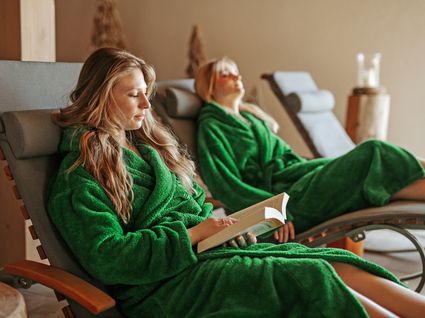 Herrliche Tageswellness in Bodenmais Zwei Frauen entspannen im Ruheraum auf Liegen im Wellnesshotel Hofbräuhaus Bodenmais – Erholung und Lesegenuss im Bademantel