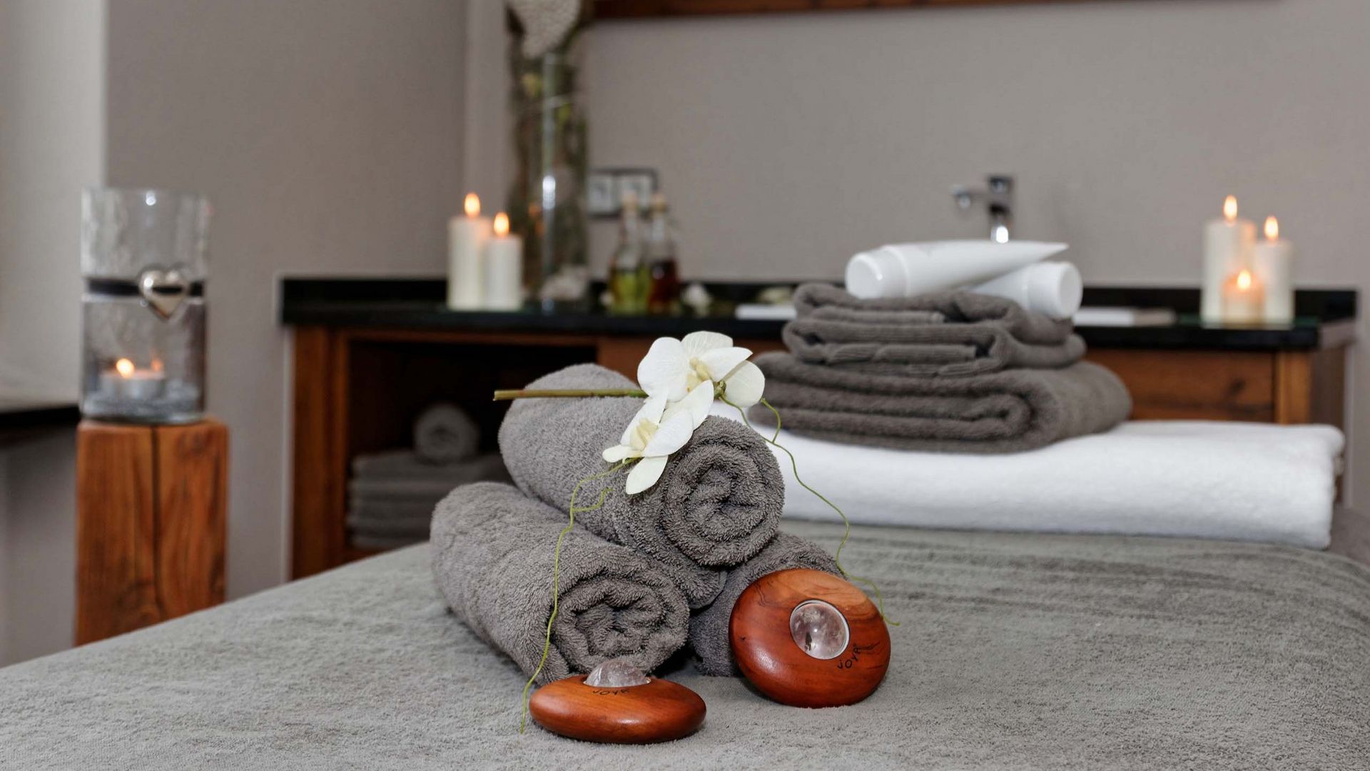 Wellnessurlaub in Bodenmais: Pauschalangebote Massageraum mit gerollten Handtüchern, Orchidee und Kerzen – entspannende Atmosphäre im Wellnesshotel Hofbräuhaus Bodenmais