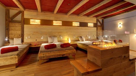 Entspannung im Bayerischen Wald: im Wellnesshotel Hofbräuhaus Moderner Ruheraum mit Holzliegen, Kaminfeuer und warmem Licht im Wellnesshotel Hofbräuhaus Bodenmais